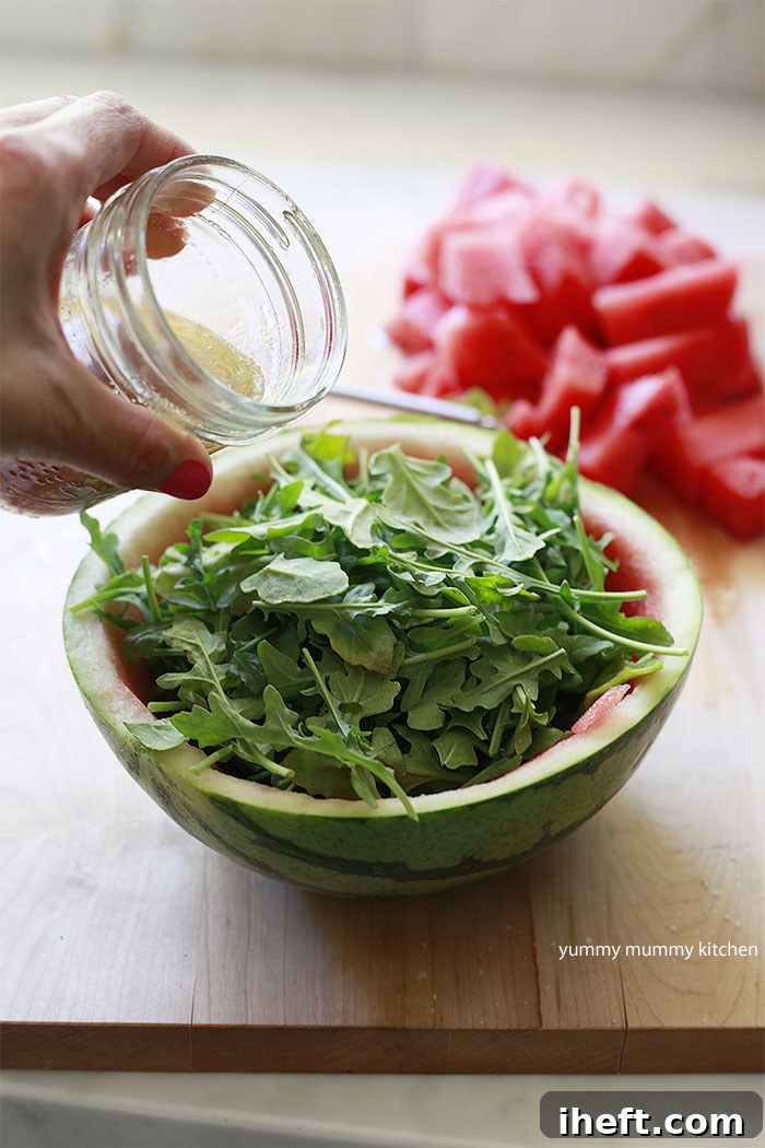 Fresh arugula being generously dressed with a homemade vinaigrette inside a hollowed-out watermelon bowl
