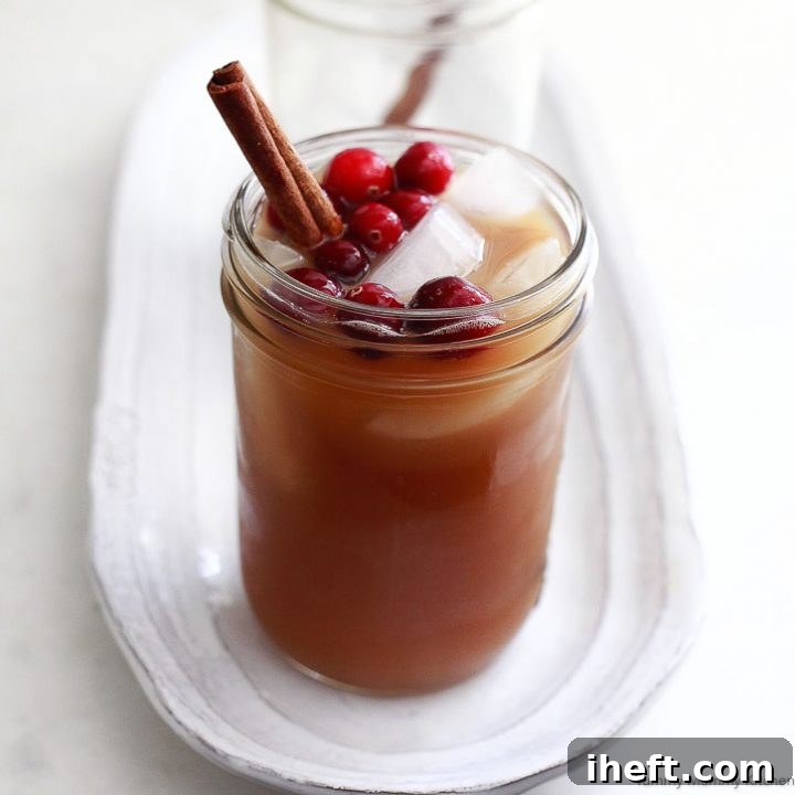 Homemade Spiced Apple Cider in a pitcher, garnished with cranberries and an orange slice.