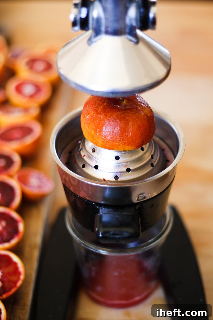 A blood orange is squeezed in a manual citrus press, illustrating the importance of fresh juice.