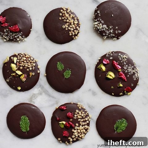 Round drops of dark chocolate topped with colorful healthy toppings like fresh mint and goji berries.