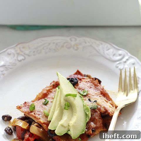 A piece of vegetarian enchilada casserole with avocado on a white plate.