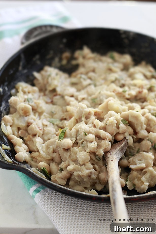 A close-up of mashing creamy white cannellini beans with fresh sage, creating a fragrant and smooth base for the dish.