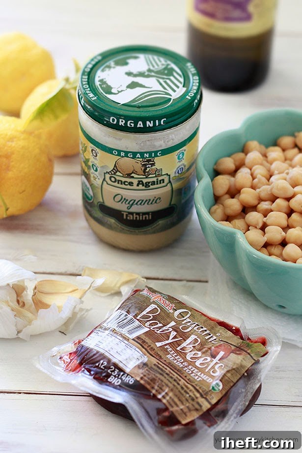 Baby beets, tahini, chickpeas, lemon, and garlic sit on a counter. These are the ingredients for homemade lemon beet hummus.