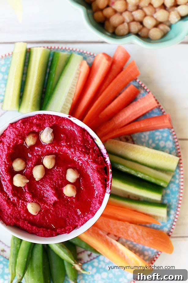 A small bowl of homemade beet hummus served with carrot sticks, cucumber, and bell pepper for a healthy snack.