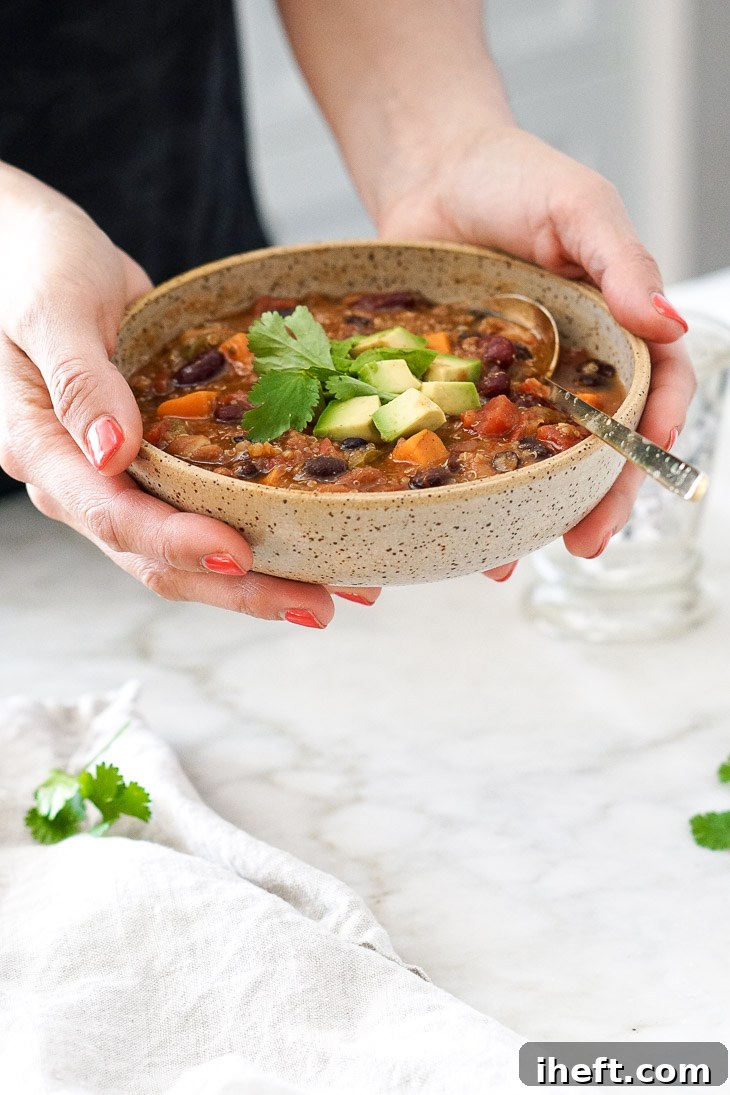 Hands holding a bowl of vibrant vegan chili topped with fresh avocado slices and cilantro sprigs. This easy vegetarian chili is perfect for the Instant Pot or slow cooker.
