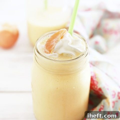 A creamy orange smoothie topped with whipped cream and an orange slice.