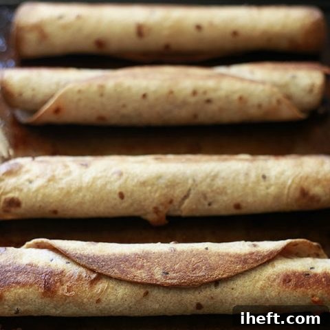 Crispy homemade vegetarian baked taquitos with bean and cheese filling on a baking sheet, ready for dipping into guacamole and salsa.