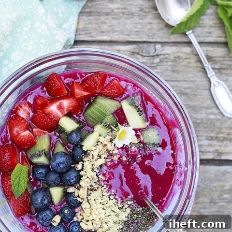 A bright pink dragon fruit or pitaya smoothie bowl generously topped with various seeds and fresh fruit slices.