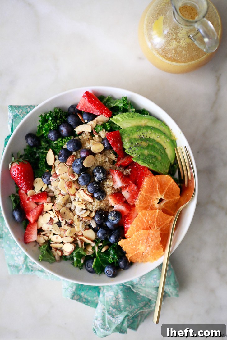A vibrant and delicious vegan kale superfood salad featuring a medley of fresh blueberries, sweet strawberries, cooked quinoa, creamy avocado, crunchy nuts, and a sprinkle of seeds. This wholesome salad is generously dressed with a bright orange vinaigrette.