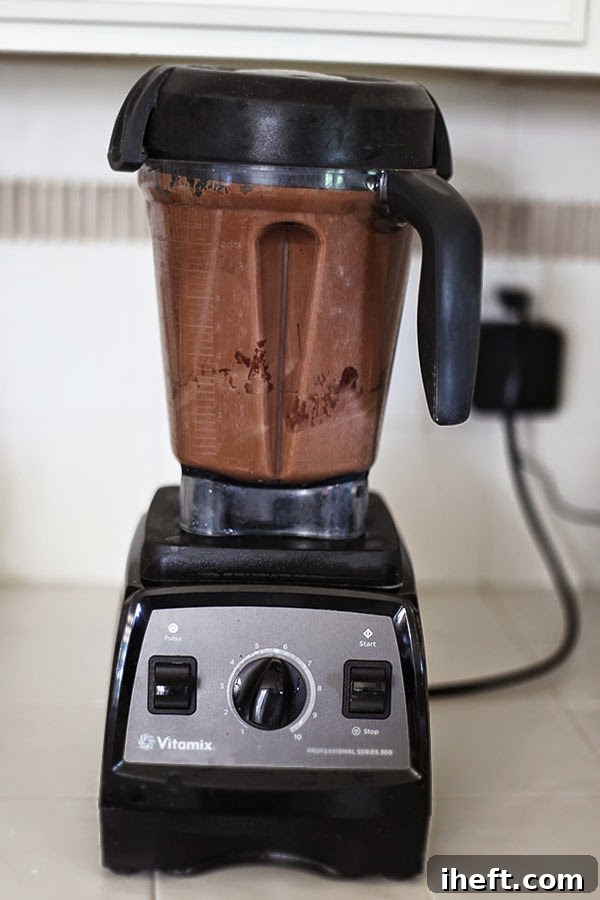 Close-up of a high-speed Vitamix blender actively mixing ingredients for a smooth, rich vegan chocolate ice cream base, demonstrating the ease of preparation.