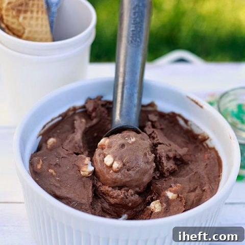 A beautifully presented bowl of creamy vegan rocky road ice cream, garnished with rich chocolate shavings, mini vegan marshmallows, and crunchy almonds, ready to be enjoyed.