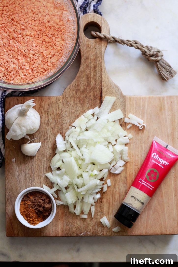 A collection of key ingredients for red lentil dal, including rinsed red lentils, freshly minced garlic, diced onion, grated ginger, and a vibrant blend of spices.