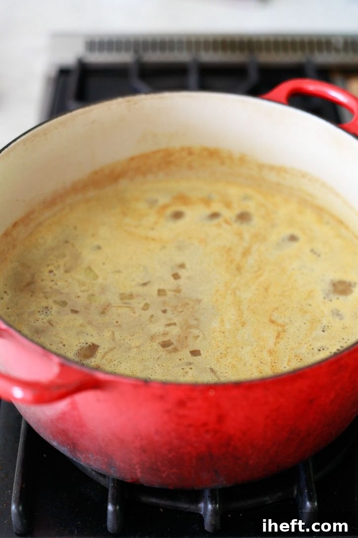 A rustic red pot on the stovetop, filled with a creamy red lentil dal beginning to gently simmer, indicating the cooking process is underway.