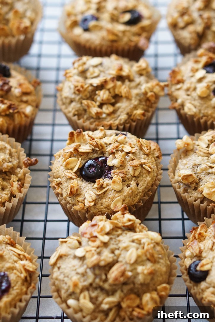 Beautifully baked granola banana muffins, dotted with blueberries, arranged on a metal cooling rack.