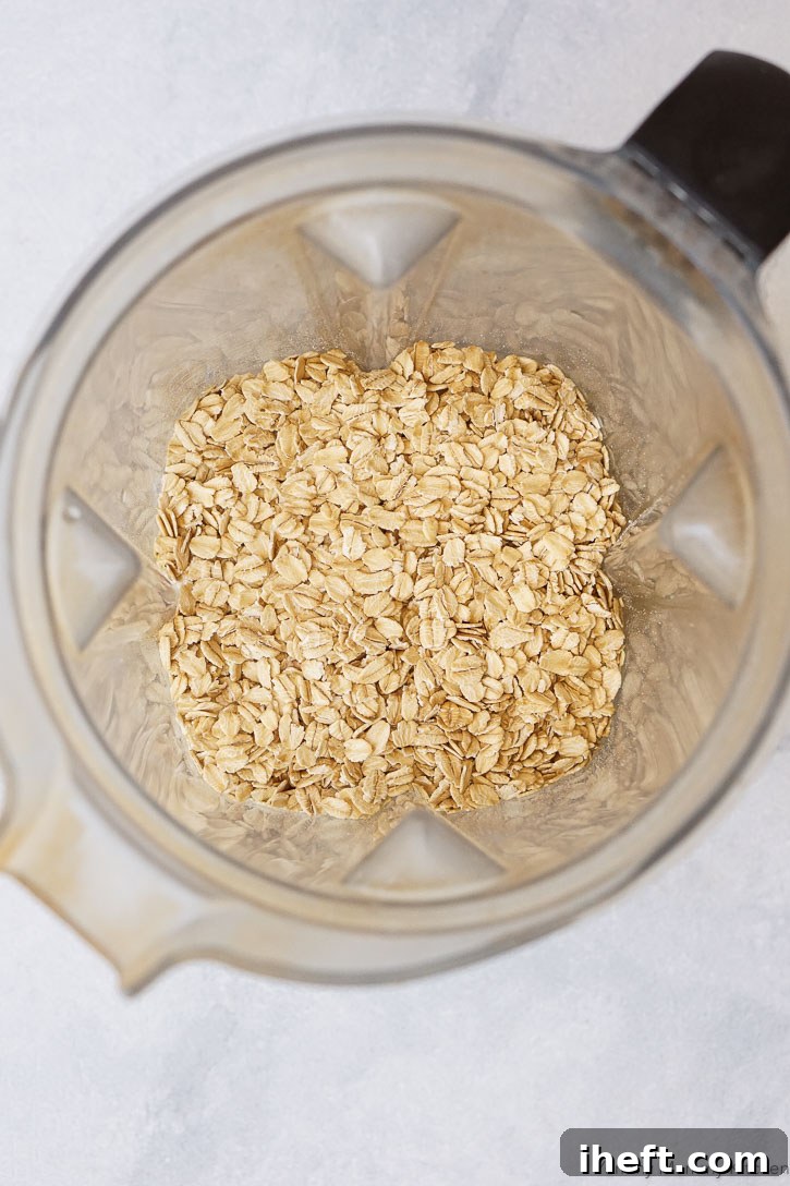 Whole old-fashioned rolled oats being poured into a Vitamix blender, ready to be ground into flour.