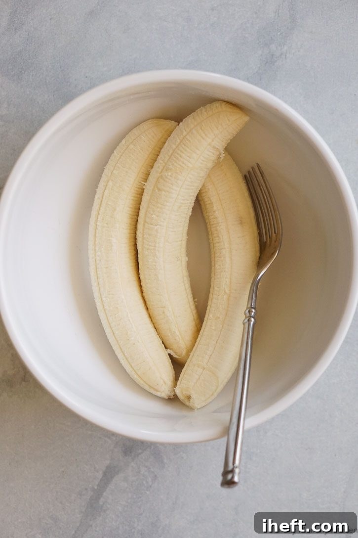 Three peeled ripe bananas arranged neatly in a white bowl, ready for mashing as the base for the muffin recipe.
