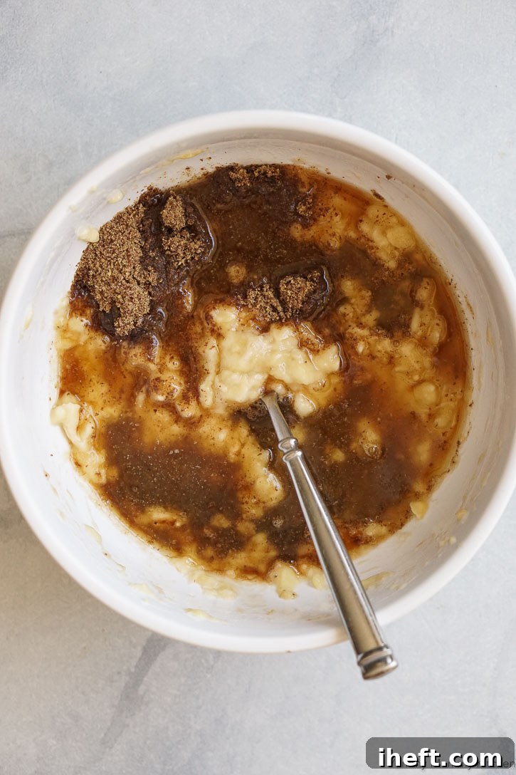 A bowl of healthy ingredients including mashed bananas, flax meal, and maple syrup, being mixed together for gluten-free banana muffins.