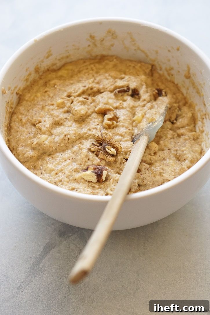 A white bowl filled with creamy, light-colored gluten-free banana muffin batter, ready for add-ins.