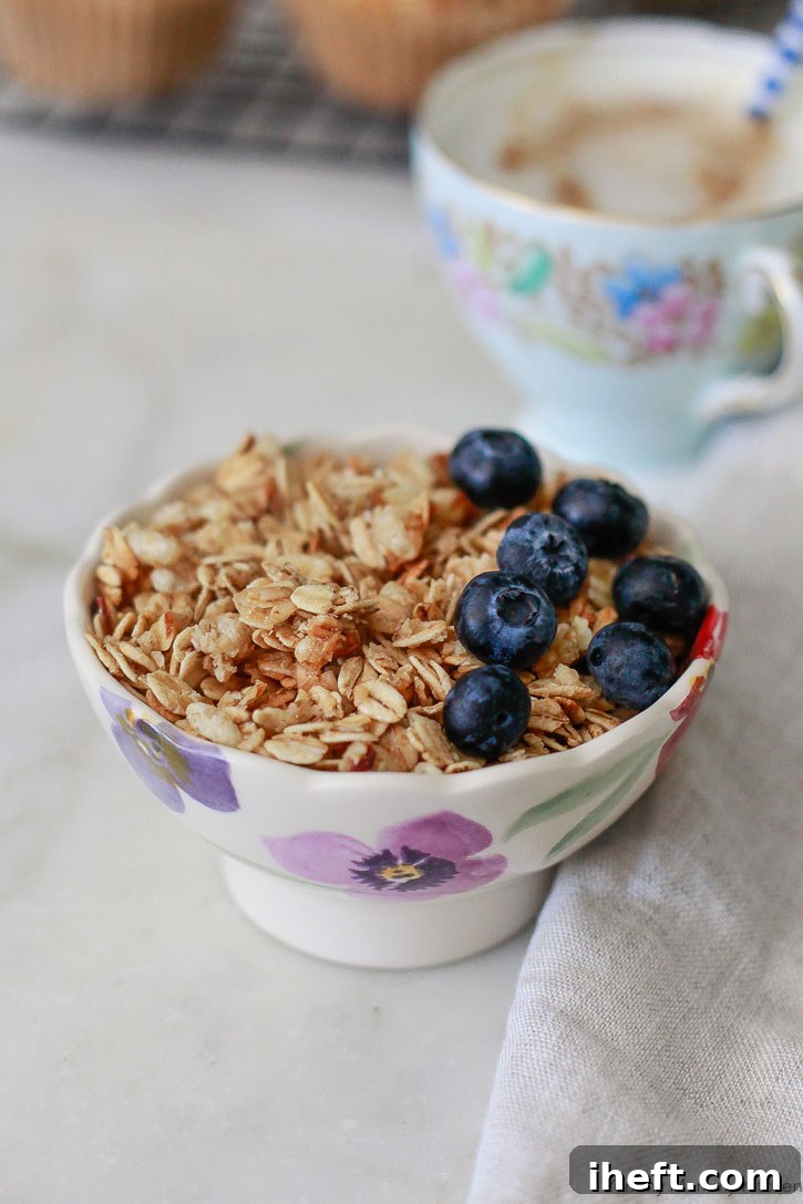 A small white bowl containing a mix of gluten-free granola and fresh, vibrant blueberries, ready to be added to muffin batter.