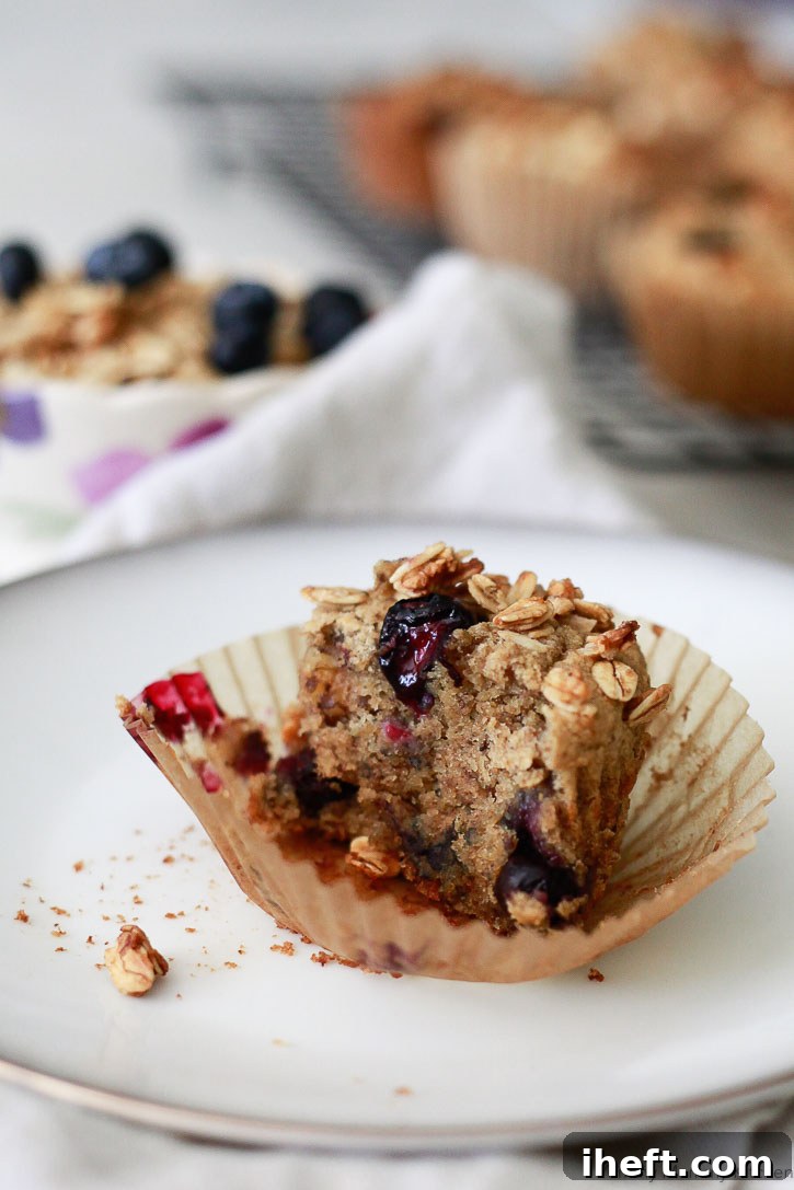A single gluten-free banana muffin, sliced in half, revealing blueberries and a granola topping, resting in a parchment baking cup.