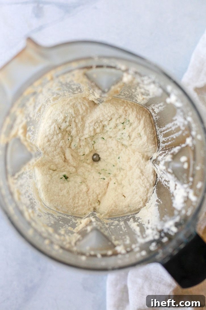 A close-up shot of creamy vegan ricotta cheese, freshly blended and ready to be used. This rich, smooth ricotta is expertly crafted from raw almonds in a blender, forming the perfect dairy-free base for a delectable vegan lasagna.