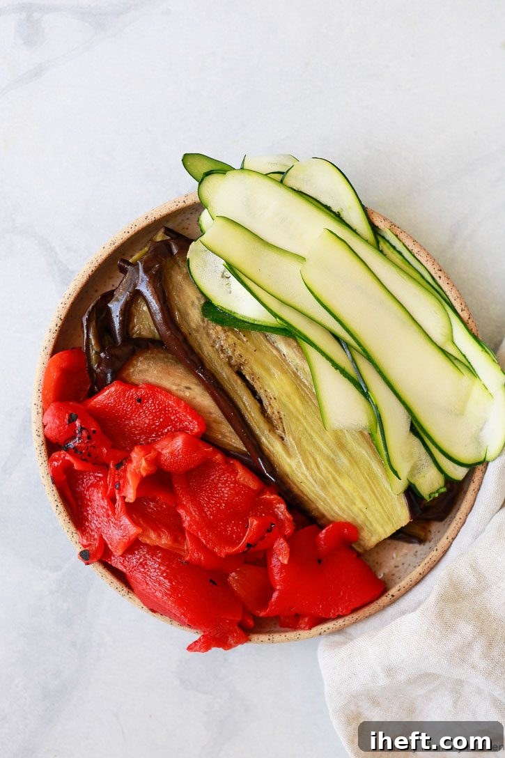 An inviting platter showcasing beautifully prepared vegetables for a vegan lasagna, featuring golden-brown roasted eggplant slices, thinly shaved zucchini strips, and vibrant roasted red peppers, all ready to be layered into the comforting dish.