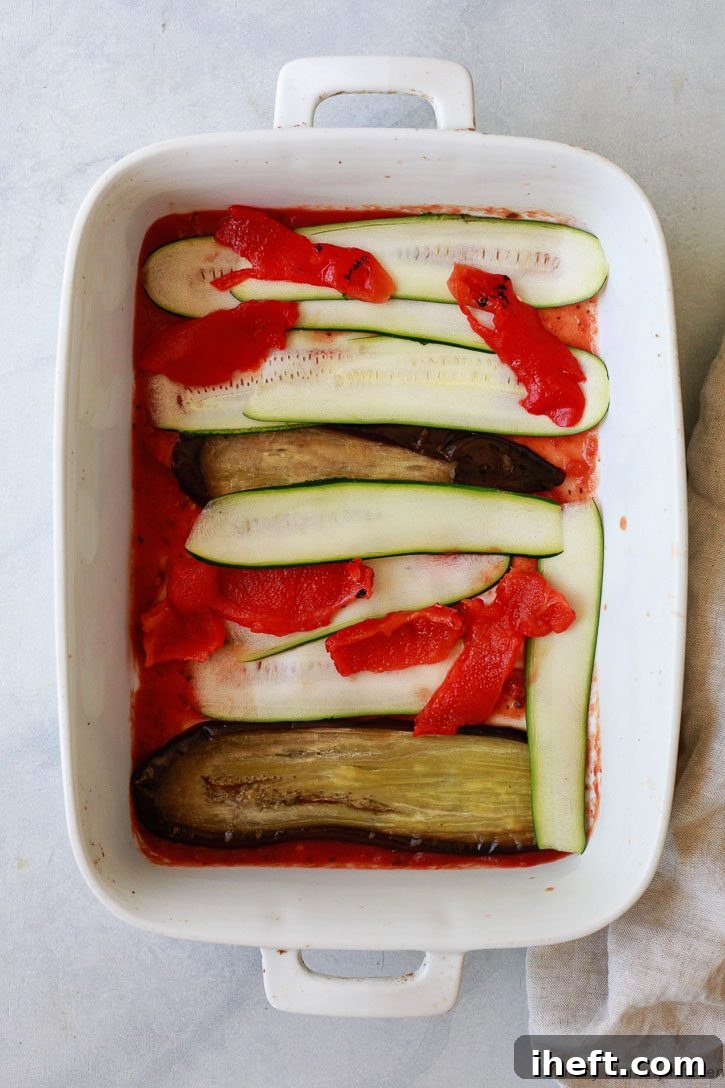 A wide shot capturing the initial stages of vegan lasagna assembly in a casserole dish, with a vibrant layer of marinara sauce spread evenly at the bottom, topped by a colorful assortment of fresh vegetables, ready for the next layer.