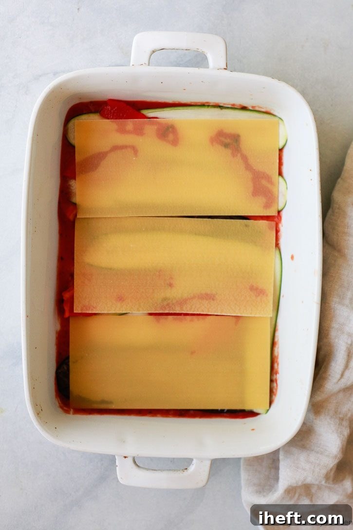A layer of no-boil lasagna noodles neatly covers the vegetables in a baking dish, forming the next crucial step in preparing this easy and delicious vegan lasagna recipe, promising convenience without compromising on taste.