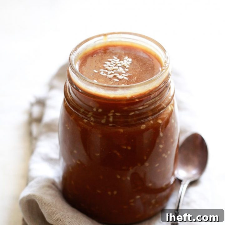 A jar of homemade teriyaki sauce with sesame seeds on a kitchen counter, ready for use.