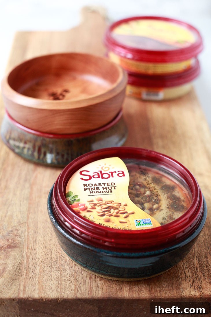Sabra's convenient 10 oz. hummus tubs are elegantly showcased, perfectly nestled within beautifully handcrafted handmade ceramic hummus bowls, highlighting a thoughtful and aesthetically pleasing presentation solution for any table.