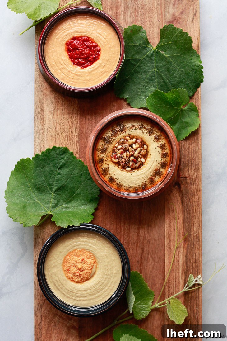 Three tubs of Sabra Hummus, artfully presented in charming handmade ceramic bowls, are arranged on a rustic wooden board and elegantly garnished with fresh grape leaves, marking the initial and crucial step in creating a truly stunning vegetarian mezze platter.