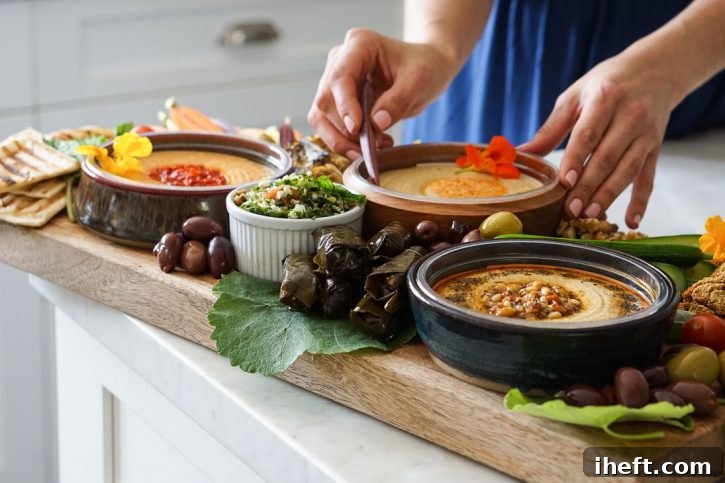 A beautifully arranged hummus platter, featuring savory stuffed grape leaves, an assortment of crisp fresh vegetables, refreshing tabbouleh salad, and briny olives, artfully presented in a bright and inviting white kitchen setting.