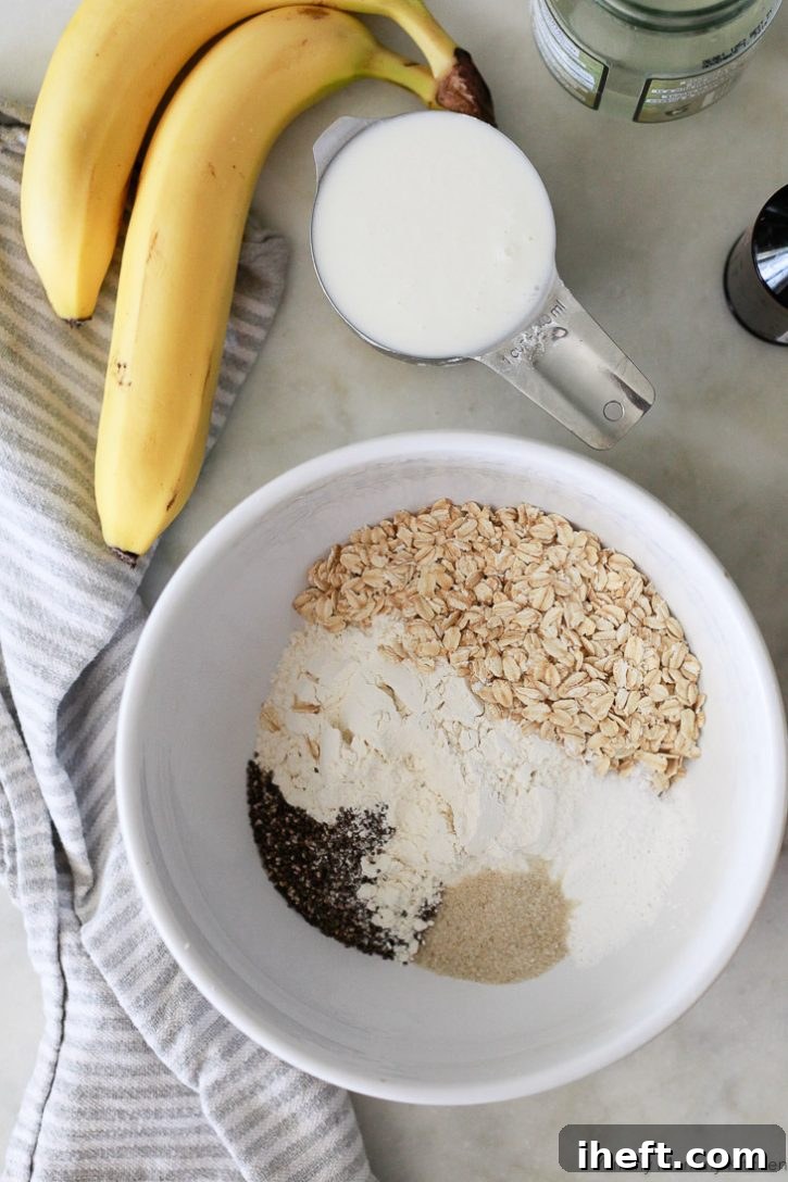 A pristine white bowl showcasing the meticulously measured dry ingredients: old-fashioned oats, all-purpose flour, baking powder for lift, organic sugar, binding chia seeds, and a pinch of sea salt, ready for whisking to create vegan banana pancakes.