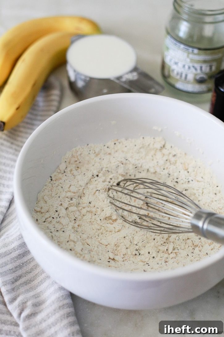 Close-up shot of dry ingredients for vegan banana pancakes being expertly whisked together in a white bowl, ensuring an even distribution of flour, oats, sugar, baking powder, salt, and chia seeds.