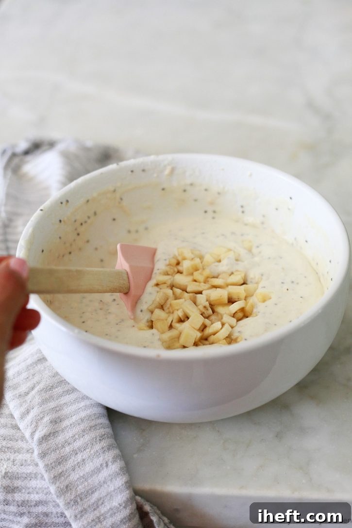 Finely diced bananas being gently folded into a luscious, thick vegan pancake batter enriched with chia seeds, ready for cooking to create a delightful breakfast.