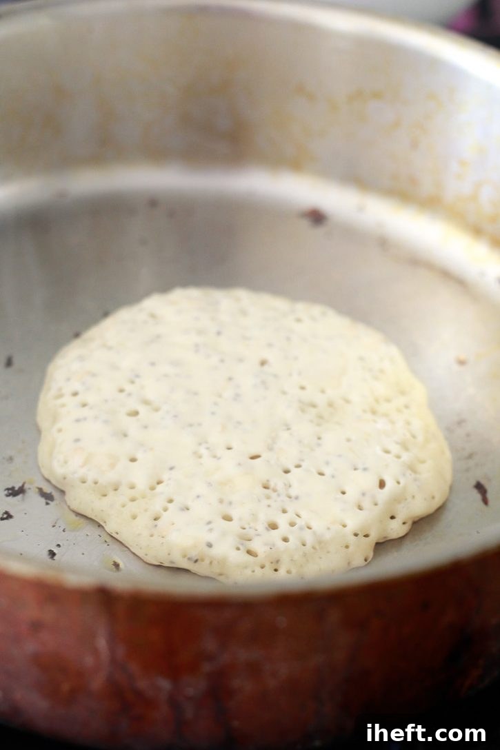A single vegan banana pancake sizzling in a hot skillet, showing bubbles forming on the surface just before being flipped, indicating it's perfectly cooking.