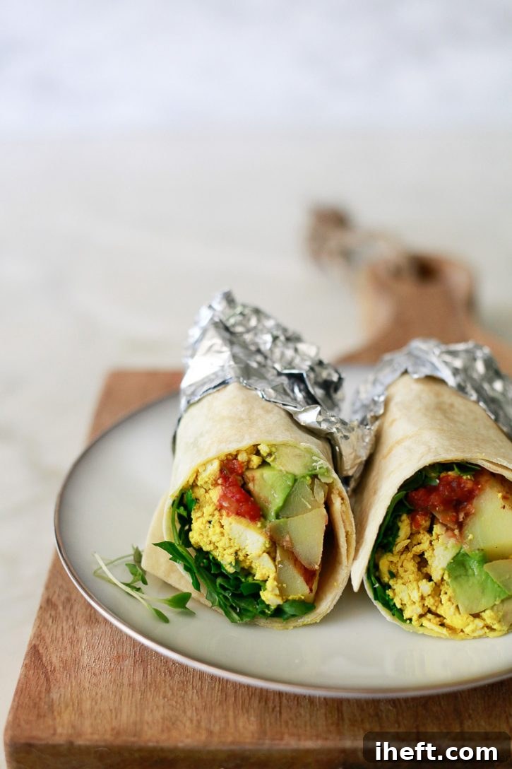 Vegan breakfast burritos filled with tofu scramble, arugula, potatoes, avocado and salsa on a white plate. 