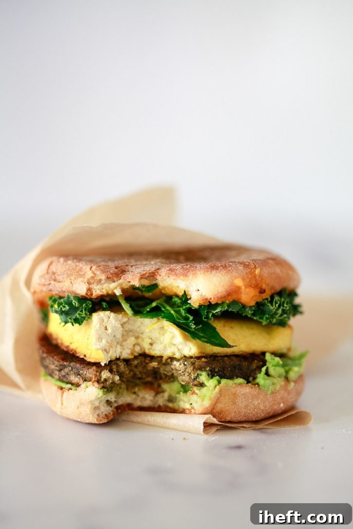A hearty close-up photo of a vegan breakfast sandwich with a bite taken out, revealing layers of plant-based goodness.