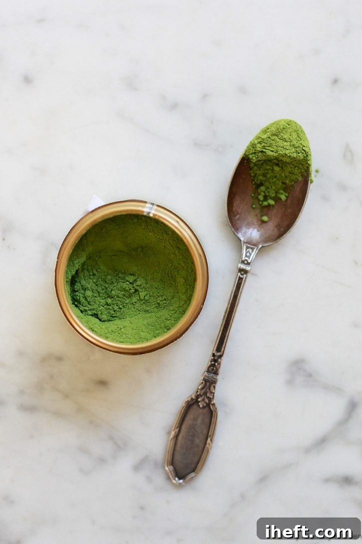 Matcha powder in a small container gets spooned out for a matcha smoothie recipe.