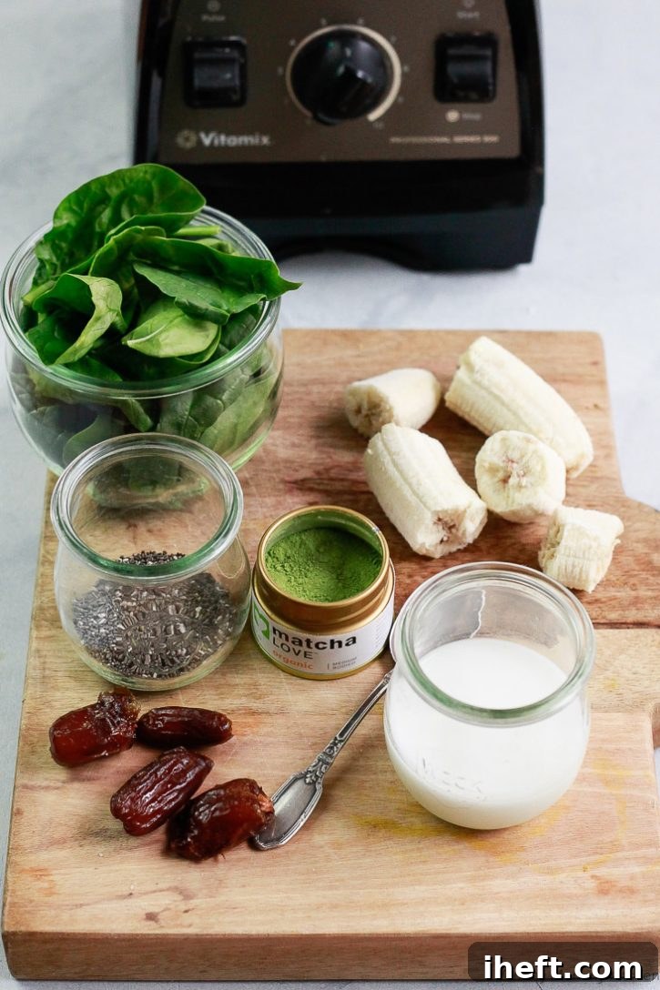 The ingredients for a healthy matcha smoothie are set on a cutting board and include almond milk, matcha powder, bananas, chia seeds, dates, and spinach.