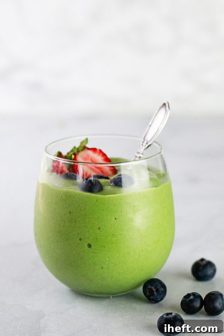 Green matcha powder smoothie in a clear glass with a spoon and berries. This healthy matcha smoothie is a delicious vegan and gluten free breakfast or snack.