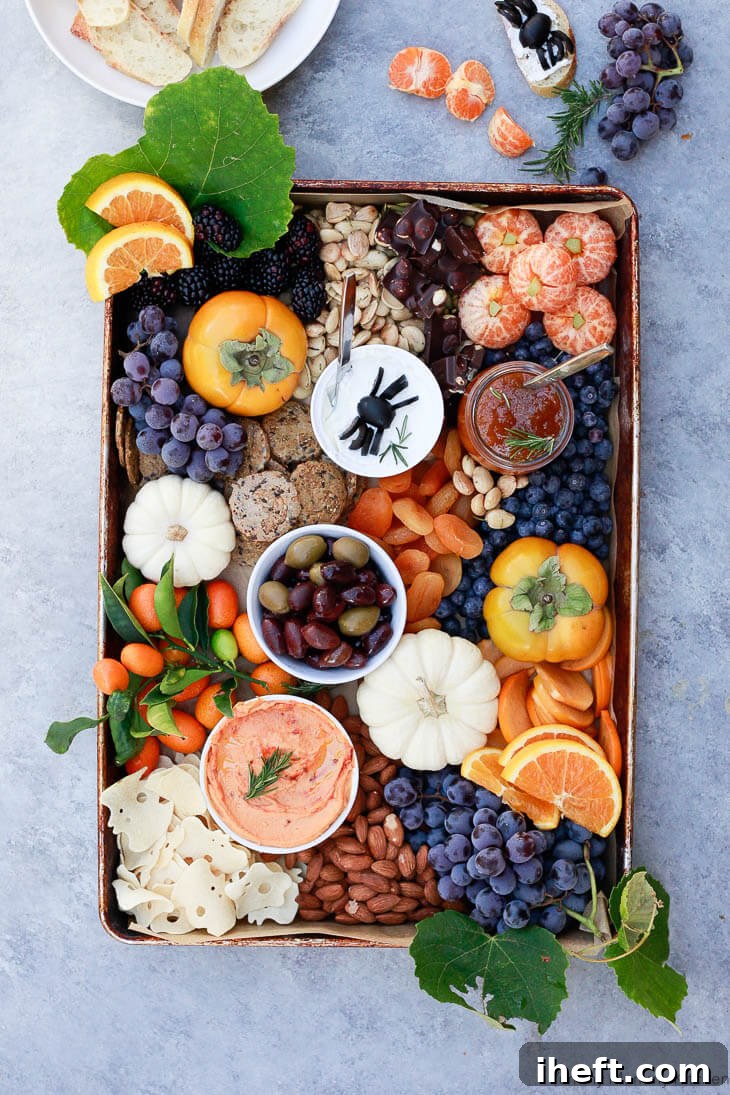 A creative Halloween party platter featuring various spooky themed snacks like cheese ghosts, pretzel spiders, and fruit arrangements.