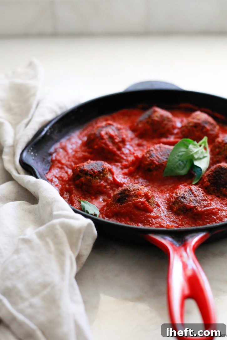 Vegan lentil meatballs in marinara sauce in a red le creuset cast iron skillet with fresh basil. 