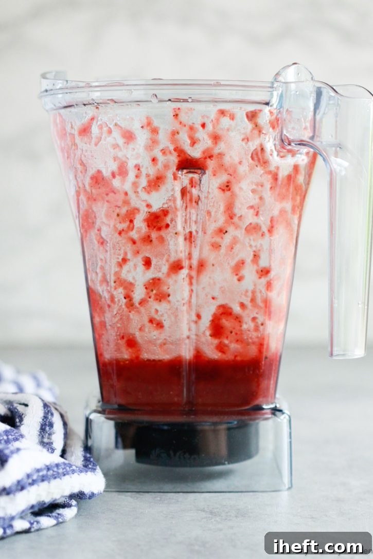 A high-powered Vitamix blender is depicted, filled with the vibrant, freshly blended homemade strawberry balsamic vinaigrette, showcasing its smooth and inviting texture.