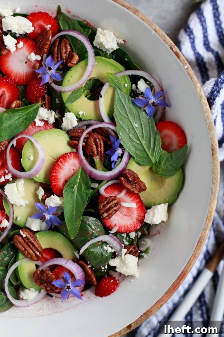 A captivating close-up photo of a beautifully composed strawberry spinach salad, featuring vibrant green basil leaves, creamy avocado slices, crunchy pecans, and crumbled feta cheese, highlighting its fresh and inviting presentation.