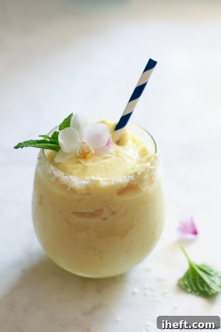 Virgin pina colada recipe garnished with fresh mint, an orchid, and a paper straw. 