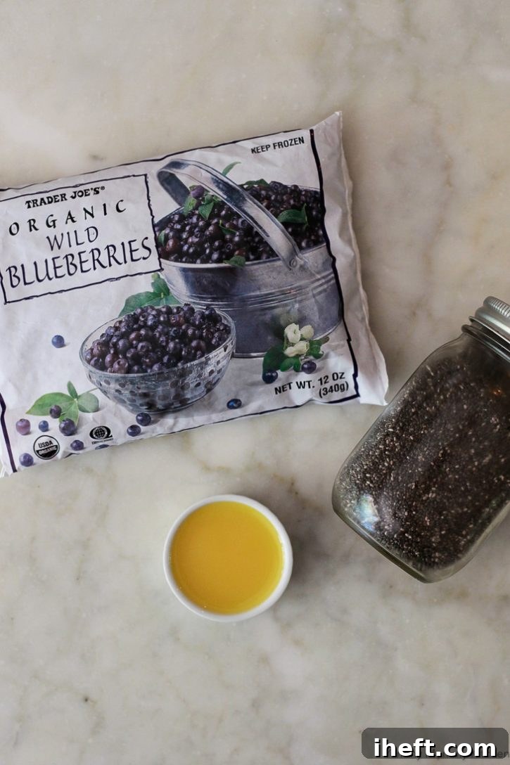 Ingredients for making healthy blueberry chia jam: a bag of frozen organic blueberries, a bottle of orange juice, and a container of chia seeds are neatly arranged.