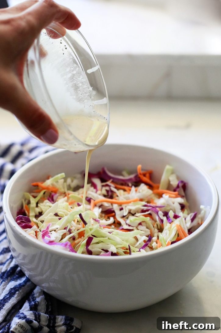 Creamy vegan coleslaw dressing being generously poured over a large bowl of vibrant shredded cabbage and carrot slaw, illustrating the easy preparation process.