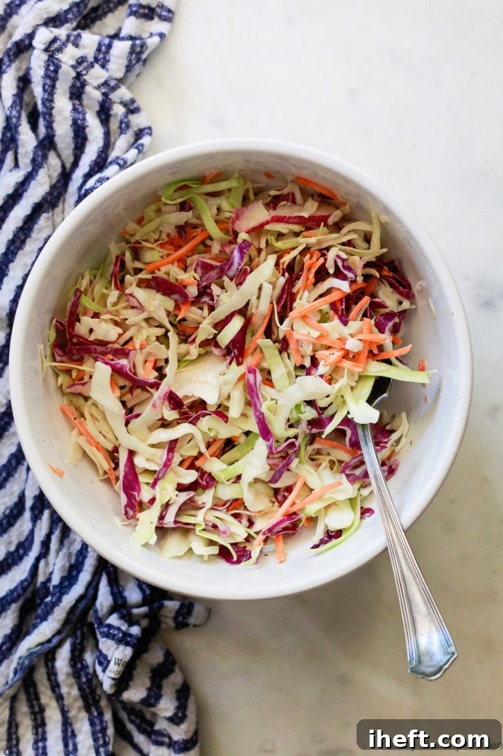 A close-up view of vibrant vegan coleslaw, featuring shredded green and red cabbage mixed with bright orange carrots and a rich, creamy vegan dressing. This classic side dish is ideal for summer BBQs and quick weeknight meals.