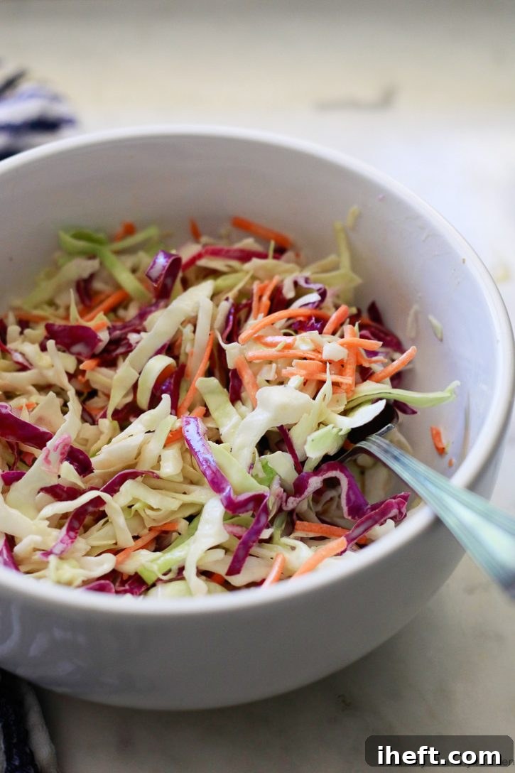 A close-up shot of a white bowl brimming with creamy vegan coleslaw, showcasing its rich texture and vibrant colors. This easy, homemade vegan coleslaw perfectly mimics the classic recipe.